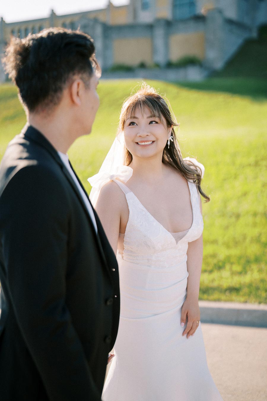 Happy bride and groom smiling at each other during outdoor wedding photoshoot with lush green background