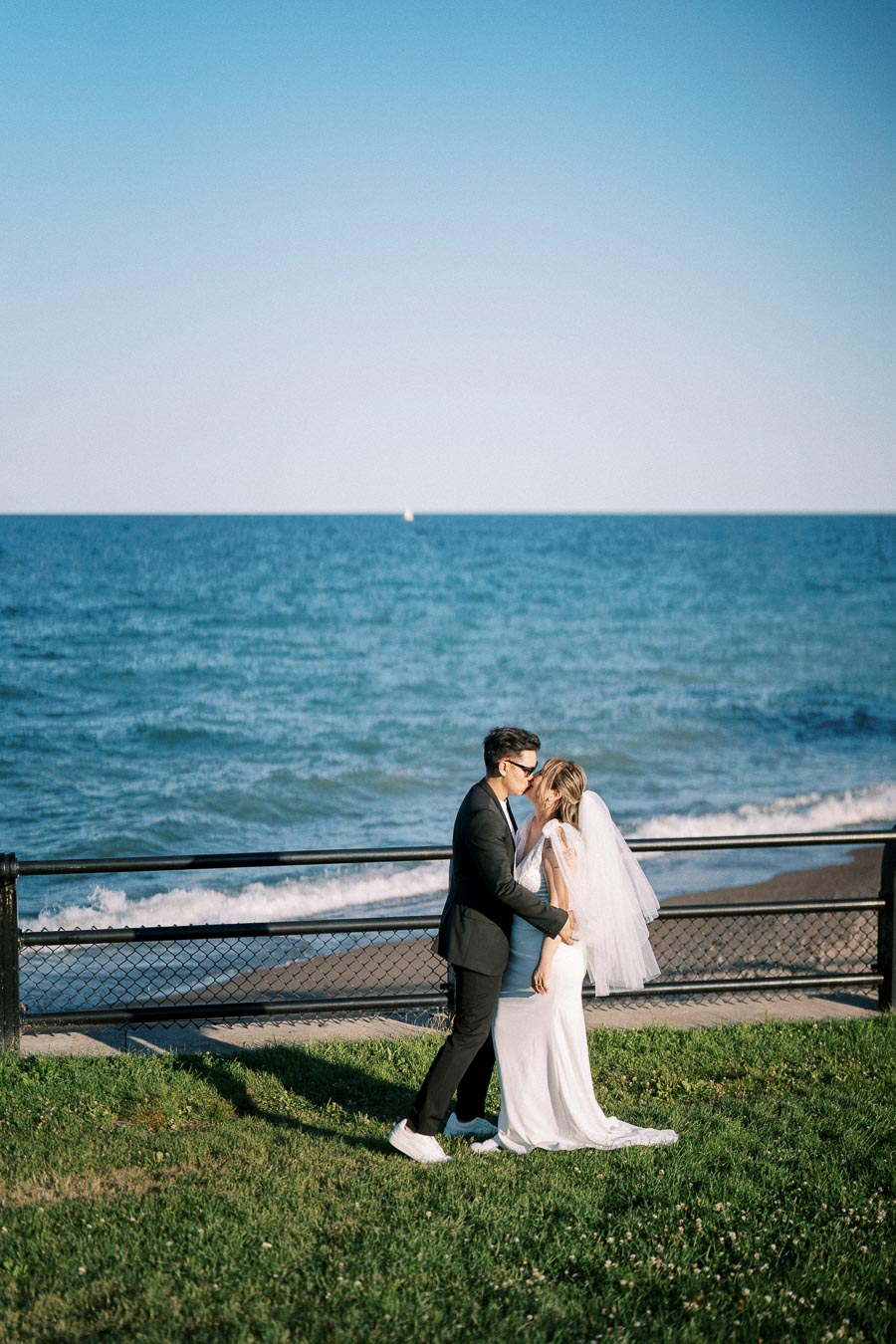 Bride and groom sharing a romantic moment by the ocean, with a blue sky and gentle waves in the background.