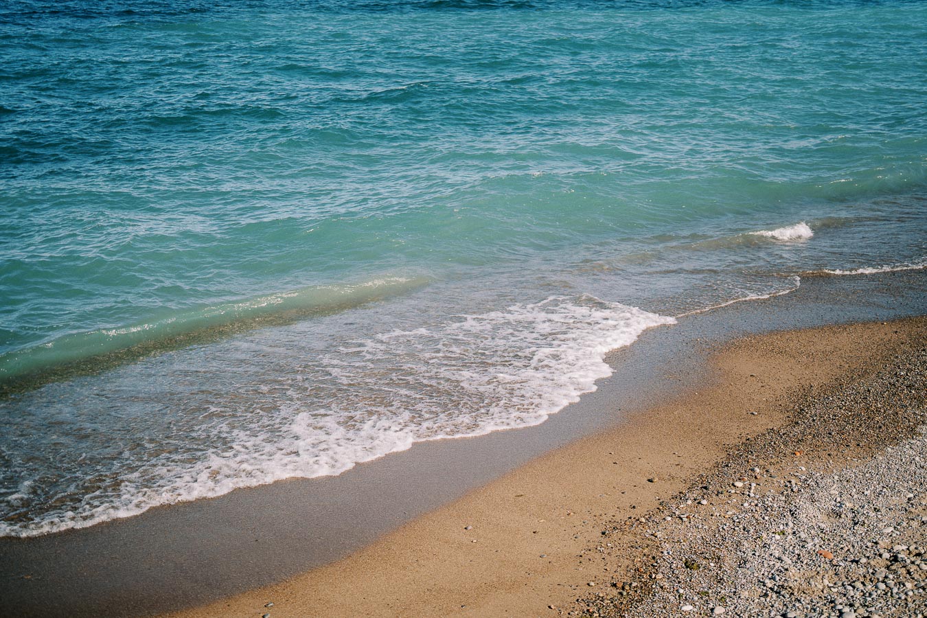 Serene beach shoreline with gentle waves lapping onto the sandy shore under a clear blue sky.