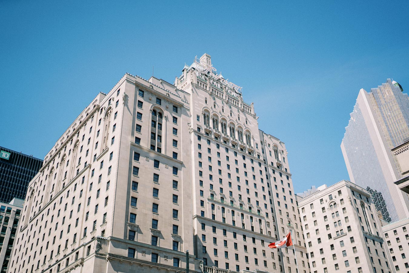 Elegant historic building with classical architecture in an urban setting, featuring a Canadian flag against a clear blue sky.