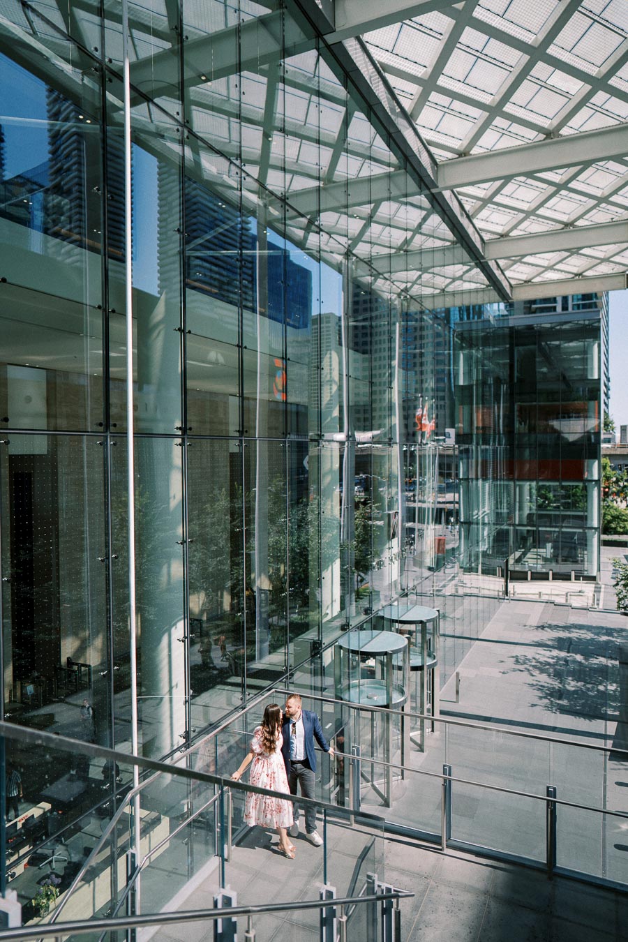 Modern architectural glass building interior with people walking, featuring sunlight reflections and cityscape view.