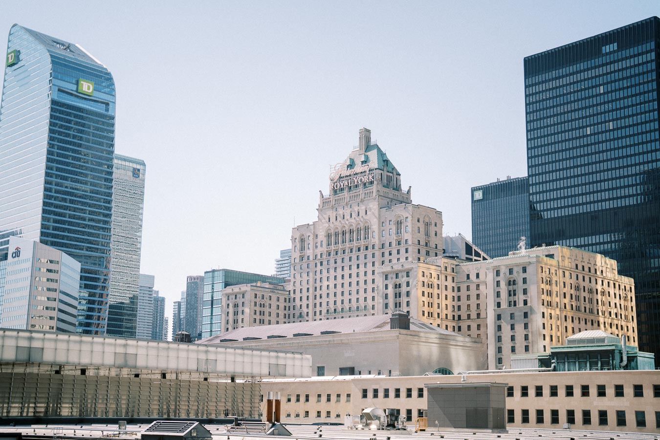 Skyscrapers and historical buildings in downtown Toronto against a clear blue sky, featuring modern architecture and classic design.