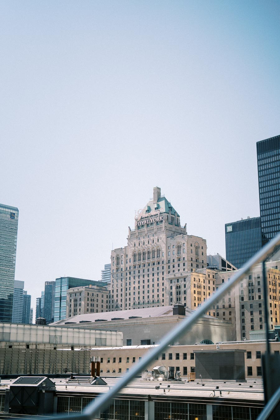 Historic hotel building with prominent signage against a clear sky, surrounded by modern skyscrapers in an urban landscape.