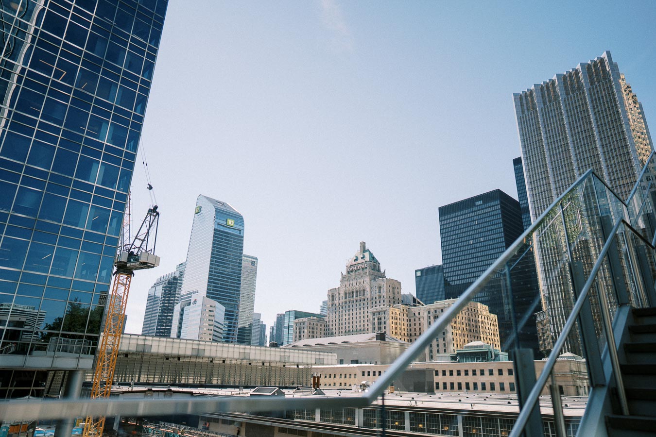 Modern city skyline with skyscrapers and blue sky, featuring glass buildings and a construction crane in the foreground.