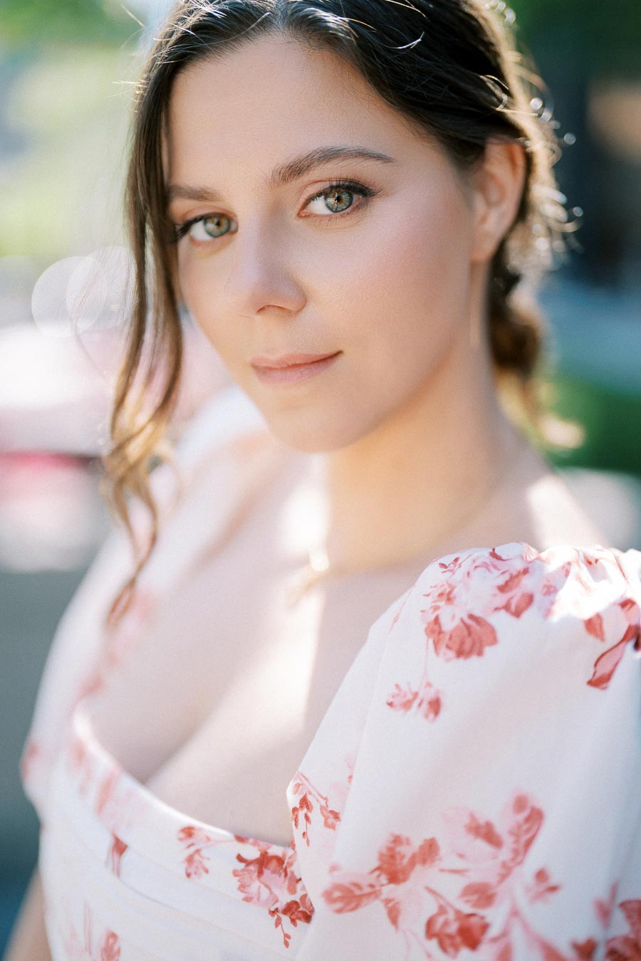 Portrait of a woman in a white dress with red floral patterns, with soft lighting highlighting her face and a blurred outdoor background.