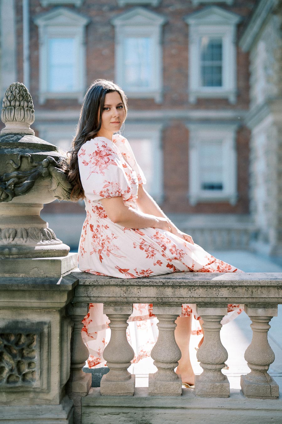 Elegant woman in floral dress seated on a stone balustrade, historical building in background