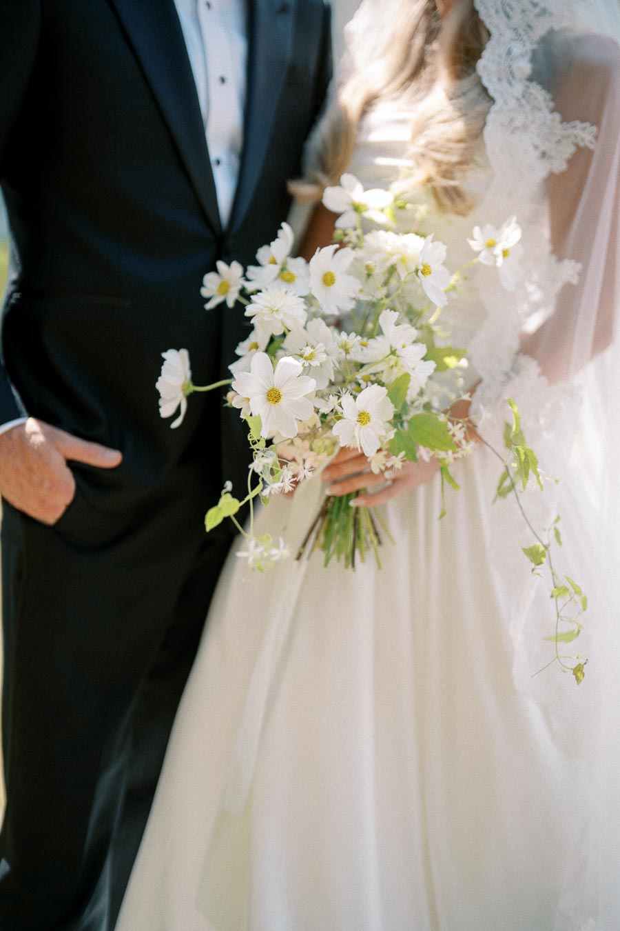 Elegant wedding couple with bride holding bouquet of white flowers and groom in black suit.