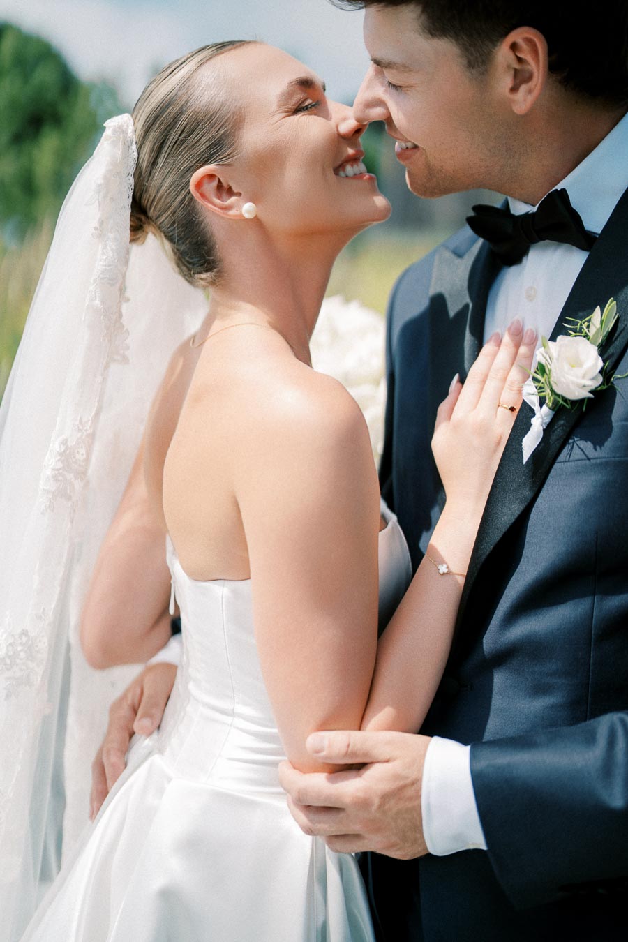 A bride and groom sharing a joyful and intimate moment on their wedding day, with the bride wearing a white gown and veil and the groom in a navy suit with a boutonniere.