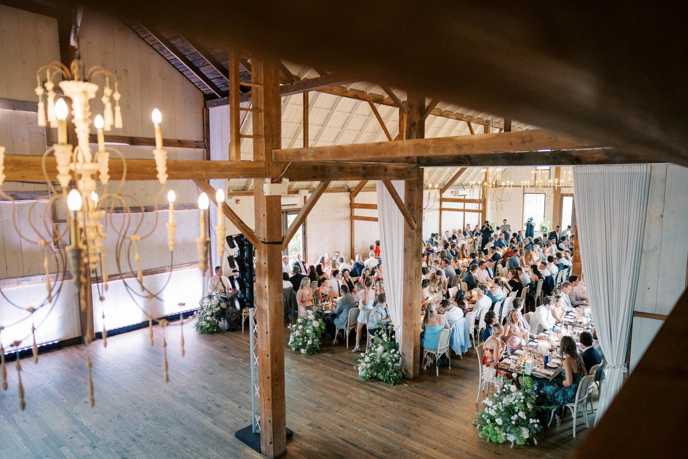 Rustic barn wedding reception with elegantly decorated tables and chandeliers, capturing guests enjoying the celebration in a cozy, wooden interior.