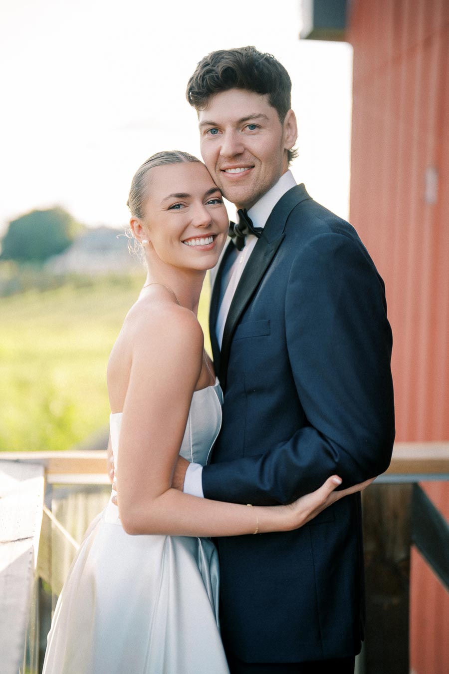 ```markdown
A joyful bride and groom embracing on their wedding day, standing on a balcony with a scenic outdoor background.
```