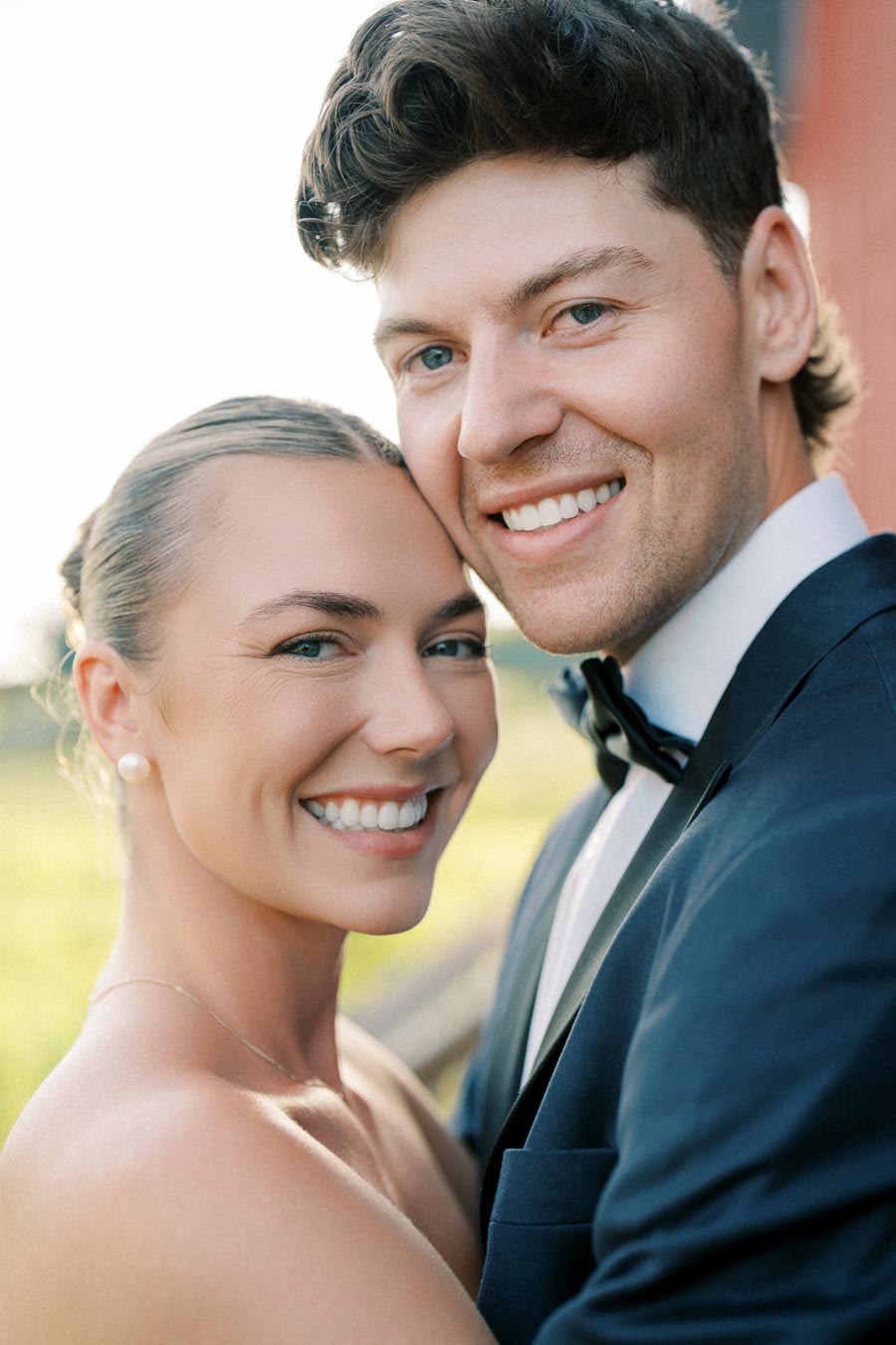 Smiling couple embracing outdoors in formal attire, with a clear blue sky in the background, capturing a joyful moment.