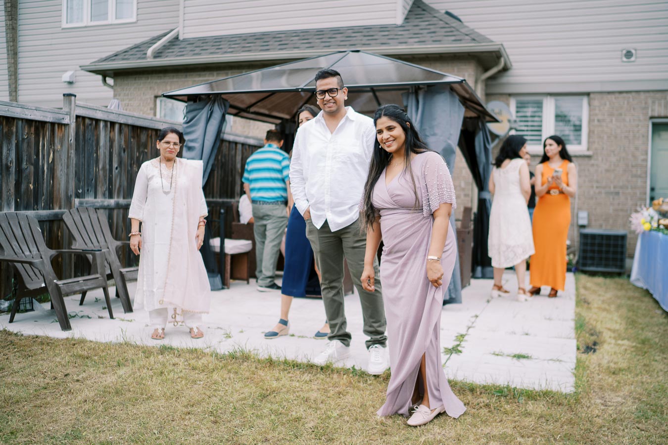 A group of people enjoying an outdoor gathering in a backyard with a gazebo, captured in a casual and friendly setting.
