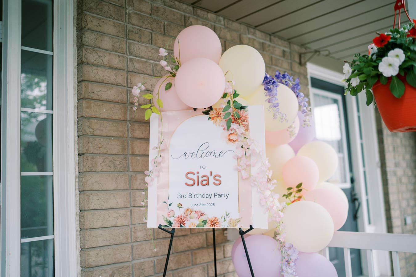 Decorative welcome sign for Sia's 3rd birthday party with pastel balloons and floral arrangements, June 21st, 2025, on a brick porch.
