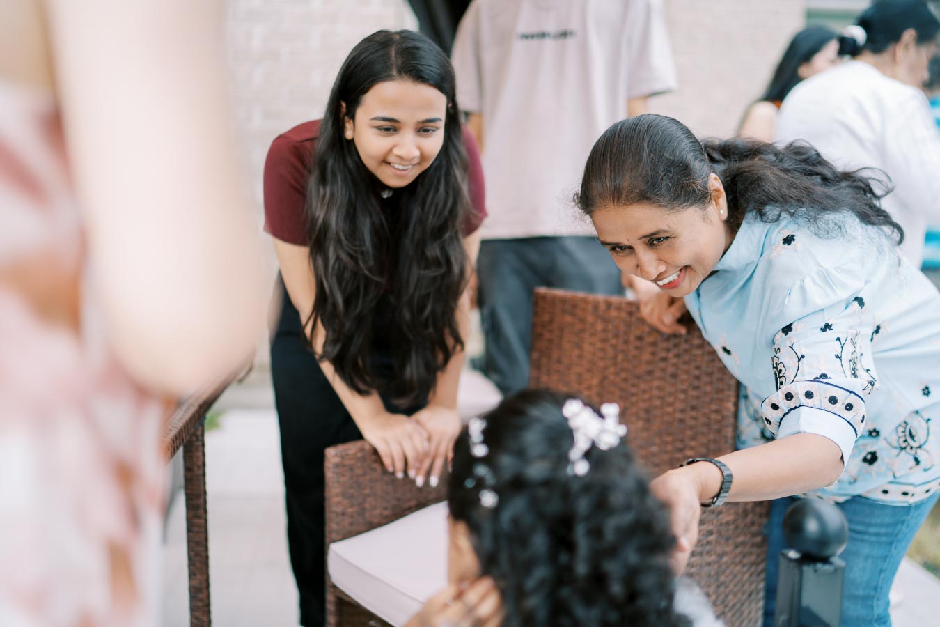 Women and children enjoying a casual outdoor gathering, smiling and engaging warmly with each other, surrounded by wicker furniture in a backyard setting.