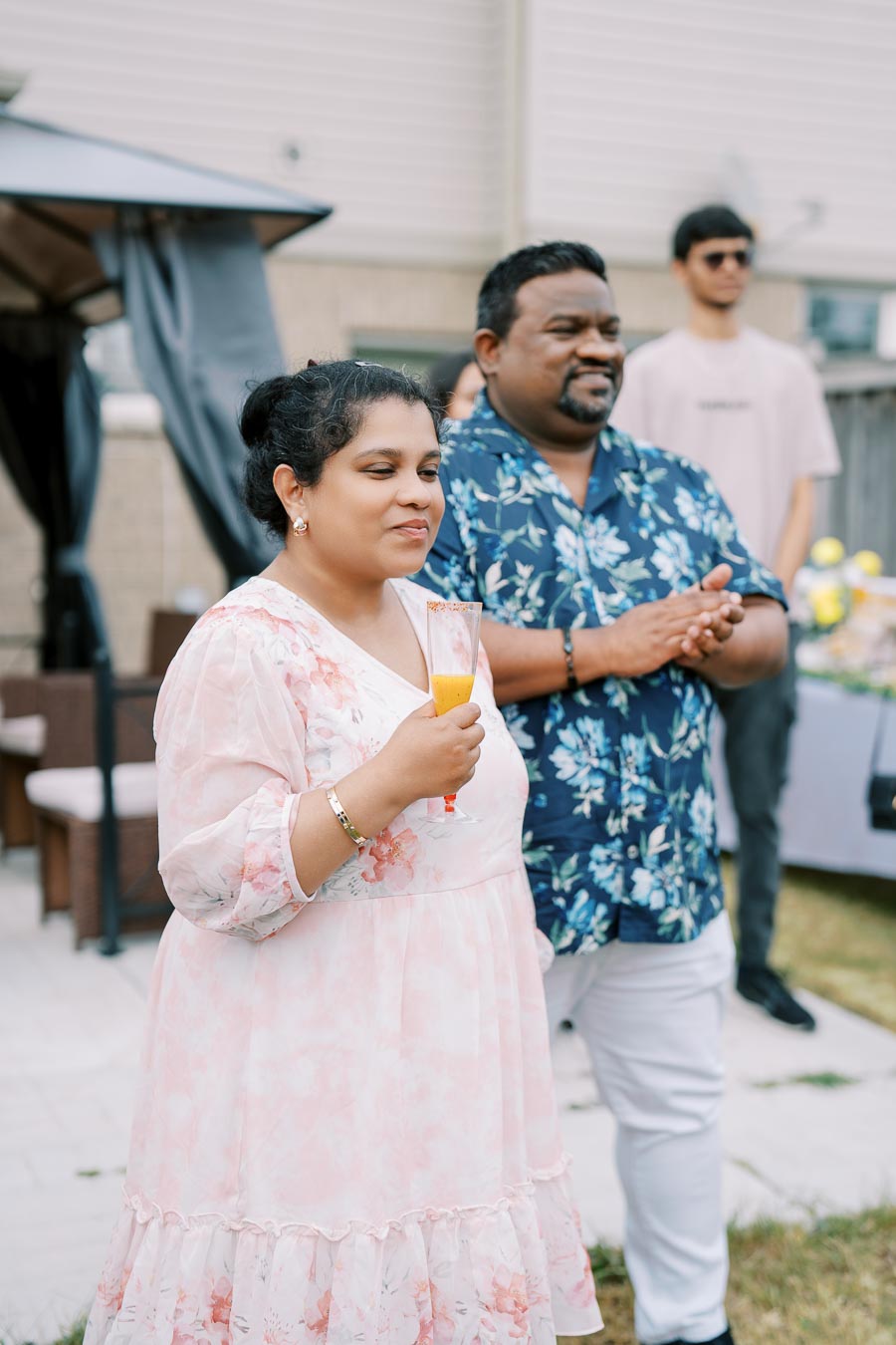 Couple enjoying outdoor gathering with drinks, dressed in floral attire, celebrating in a backyard setting