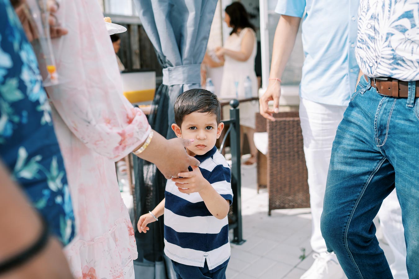 Young boy holding an adult's hand at an outdoor gathering, surrounded by casually dressed people.