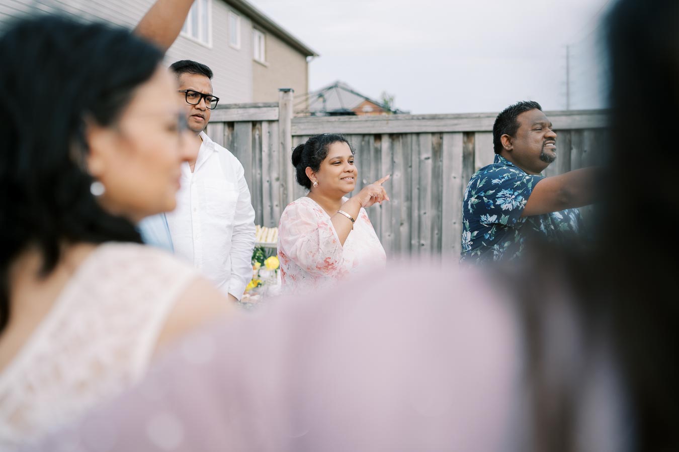 A group of people having a conversation outdoors in a backyard setting, with a wooden fence in the background.