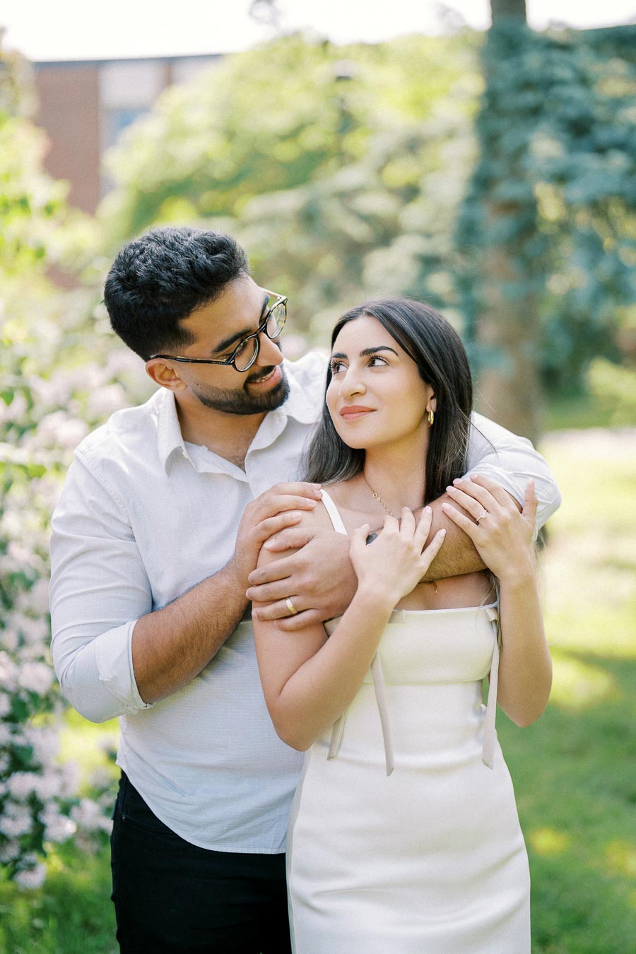 Young couple embracing in a lush green park, smiling and enjoying a sunny day, perfect for engagement or wedding photography.