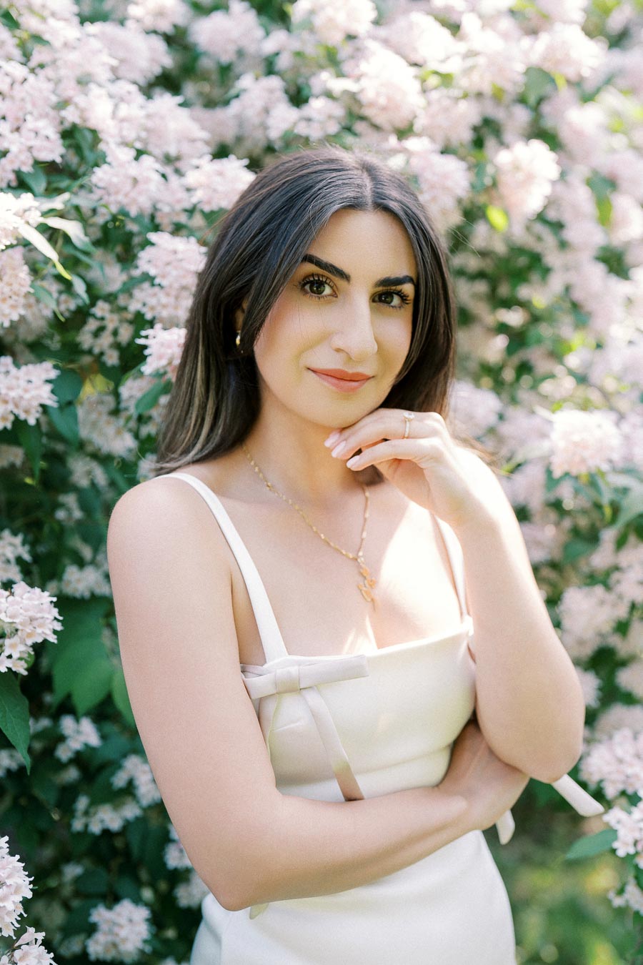 A woman in a white dress poses confidently among blooming pink flowers, showcasing a serene and elegant look.