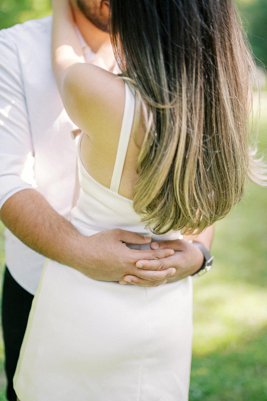 A couple sharing an intimate embrace outdoors, with the focus on their close connection and the woman's long, flowing hair. The background features a lush, green setting that complements the romantic mood.
