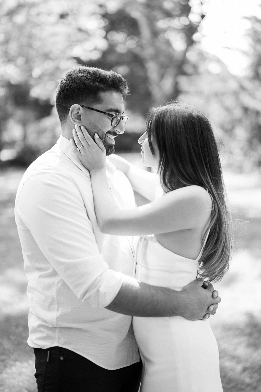 A couple embraces lovingly in a sunny outdoor setting, with the woman touching the man's face. The black and white photograph captures a romantic and intimate moment.