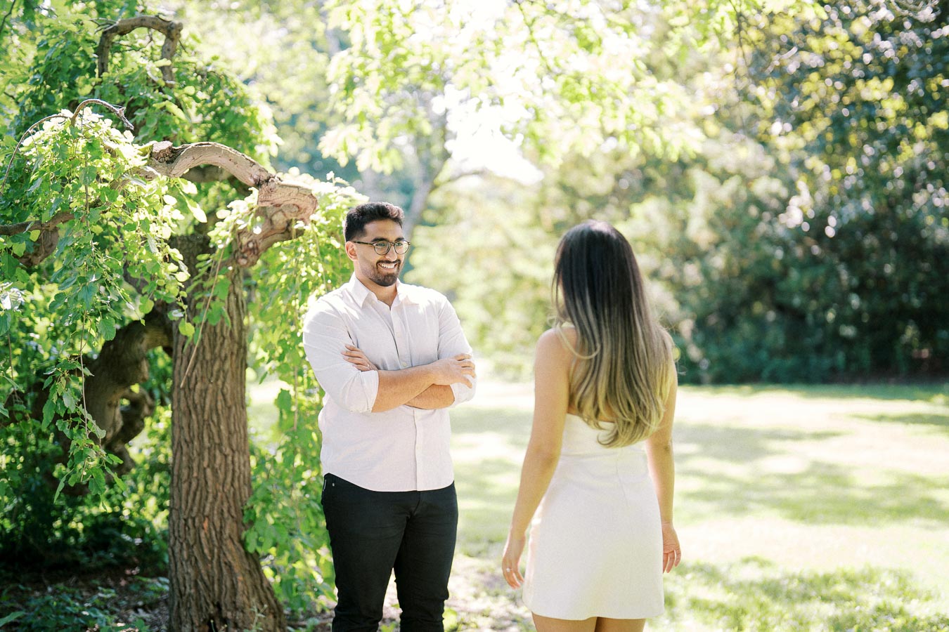 Man and woman talking in a sunny park setting, surrounded by lush greenery and a uniquely twisted tree.