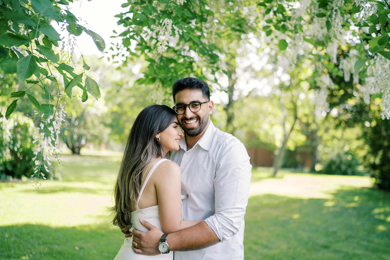 A happy couple embracing under lush green trees in a sunny park, with dappled sunlight creating a warm and romantic atmosphere.