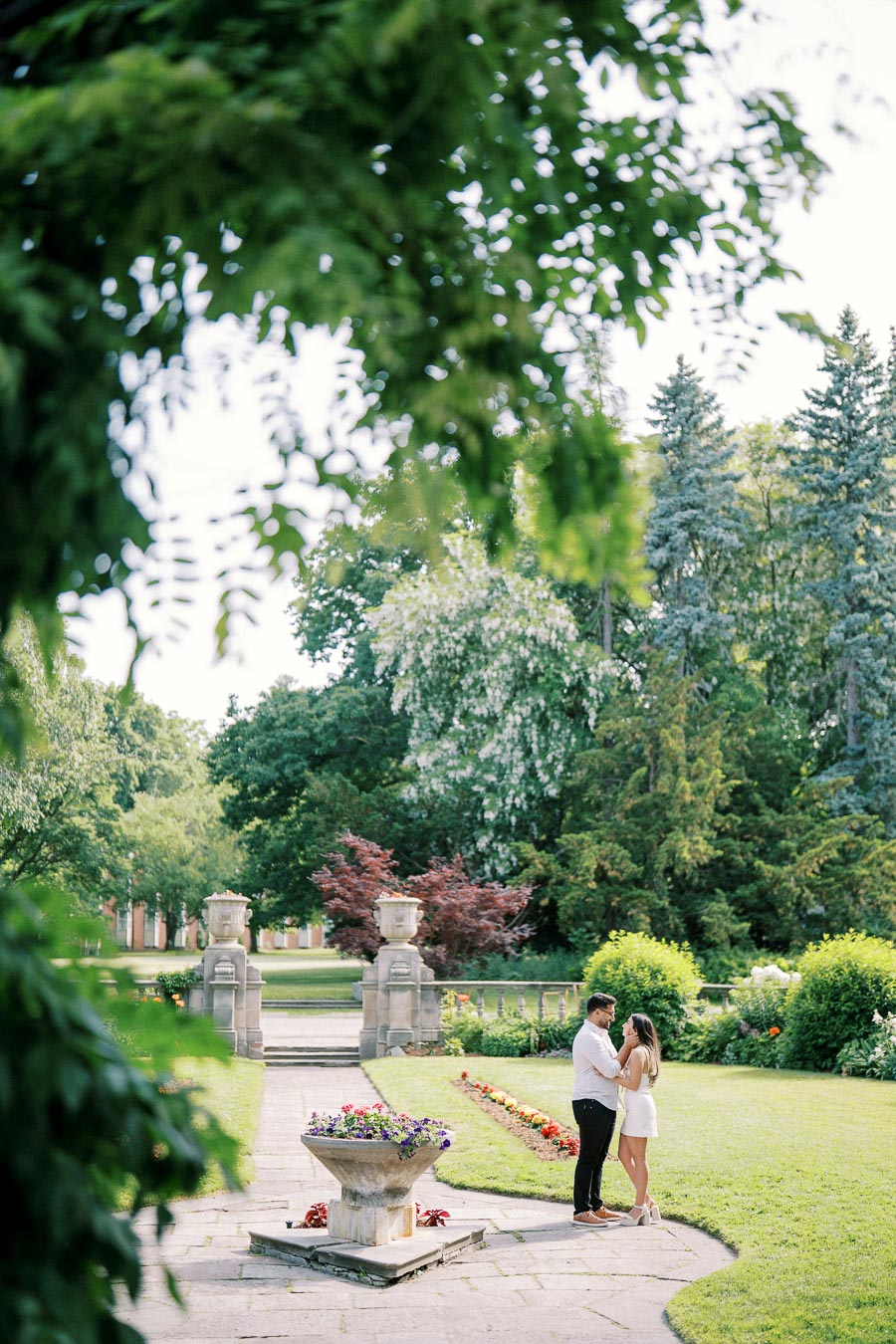 Romantic couple embracing in a lush garden with vibrant greenery and colorful flowers surrounded by elegant stone structures.