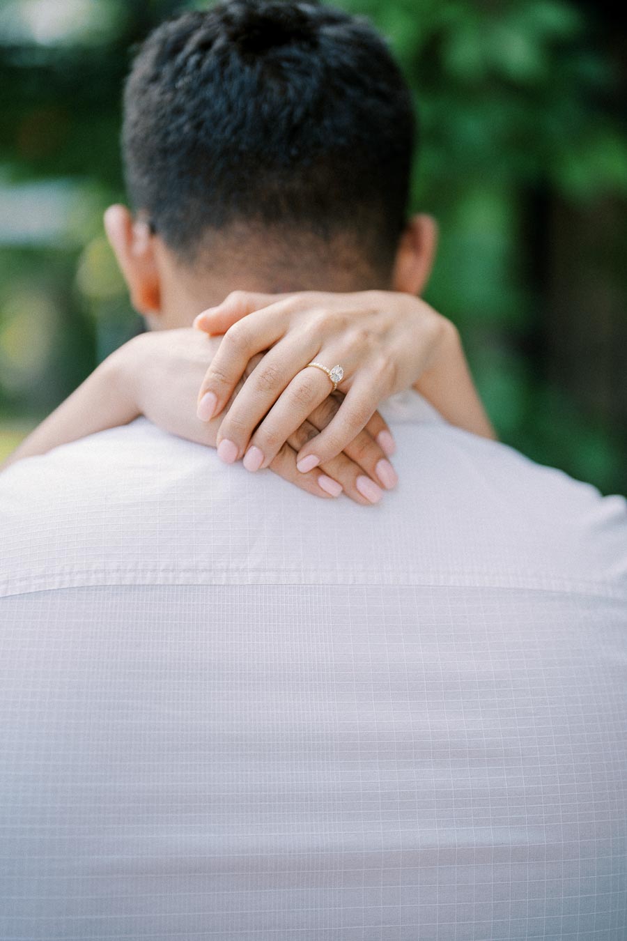 Couple embracing with woman's hands resting on partner's back, showcasing an elegant engagement ring with a diamond.