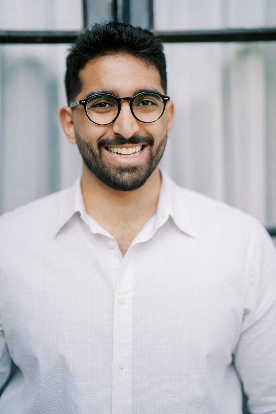 Smiling man with glasses wearing a white shirt in front of blurred background.