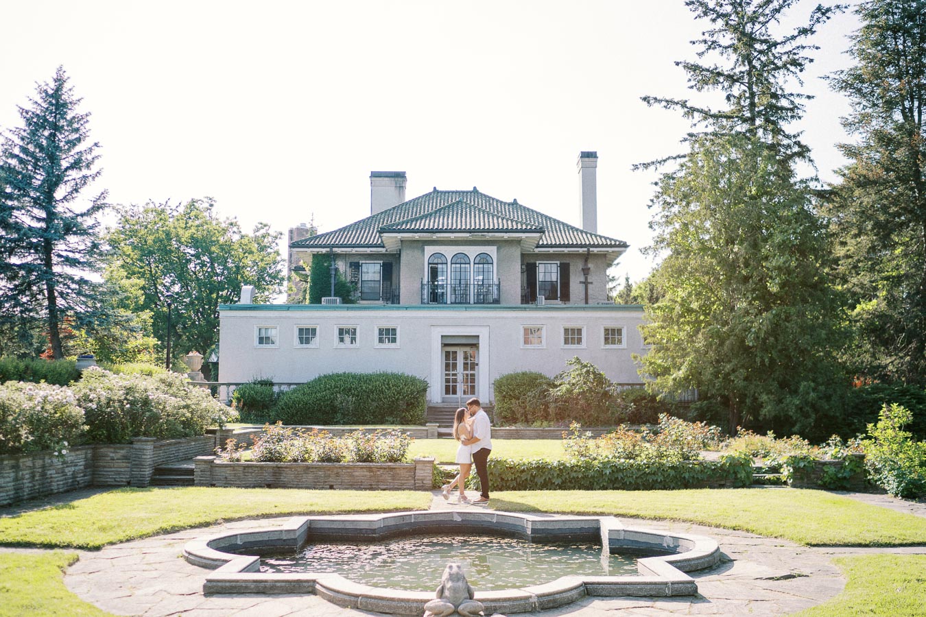 Elegant historic mansion with garden and fountain, couple embracing in foreground.