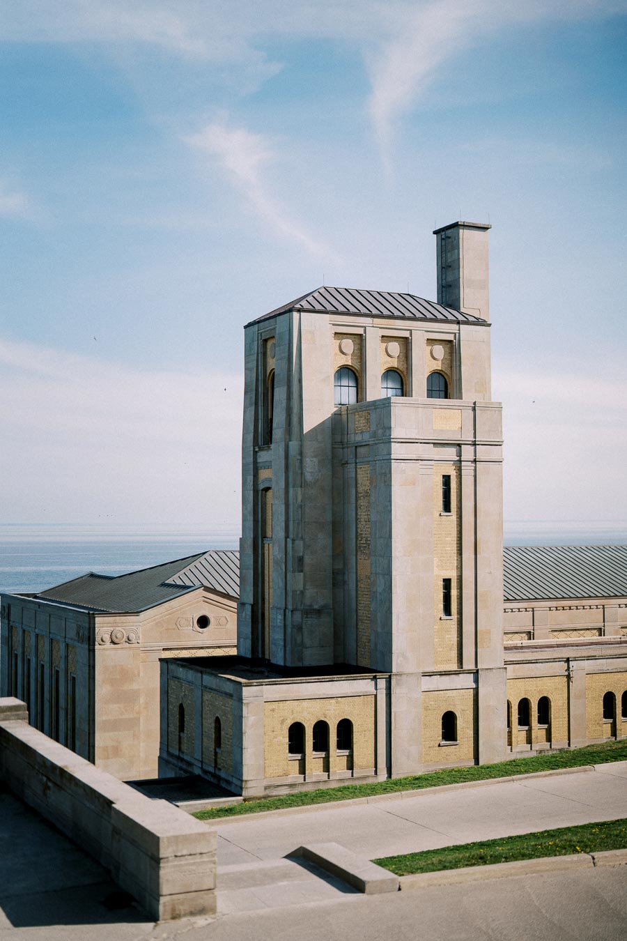 Historic stone building with tower overlooking a scenic coastline under a clear blue sky