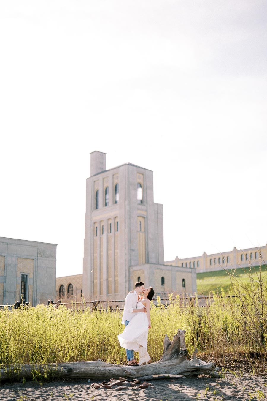 A romantic couple embracing in a lush garden setting with historic stone buildings in the background, capturing a timeless and elegant moment.