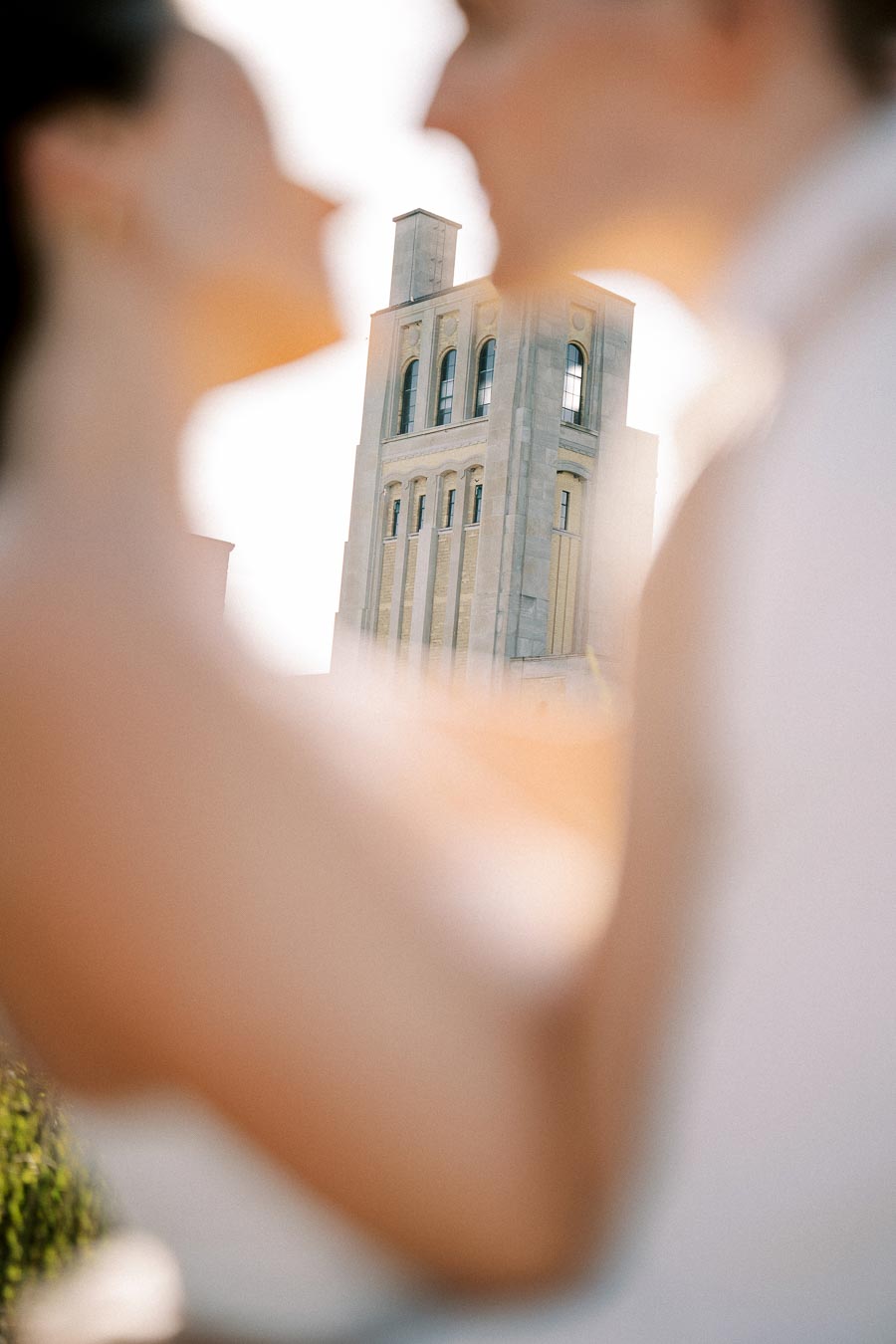 A tower building framed by the blurred silhouettes of a couple in focus, capturing a romantic urban scene under soft daylight.