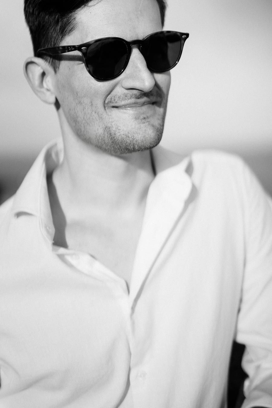 Black and white photo of a man wearing sunglasses and a white shirt, smiling confidently.