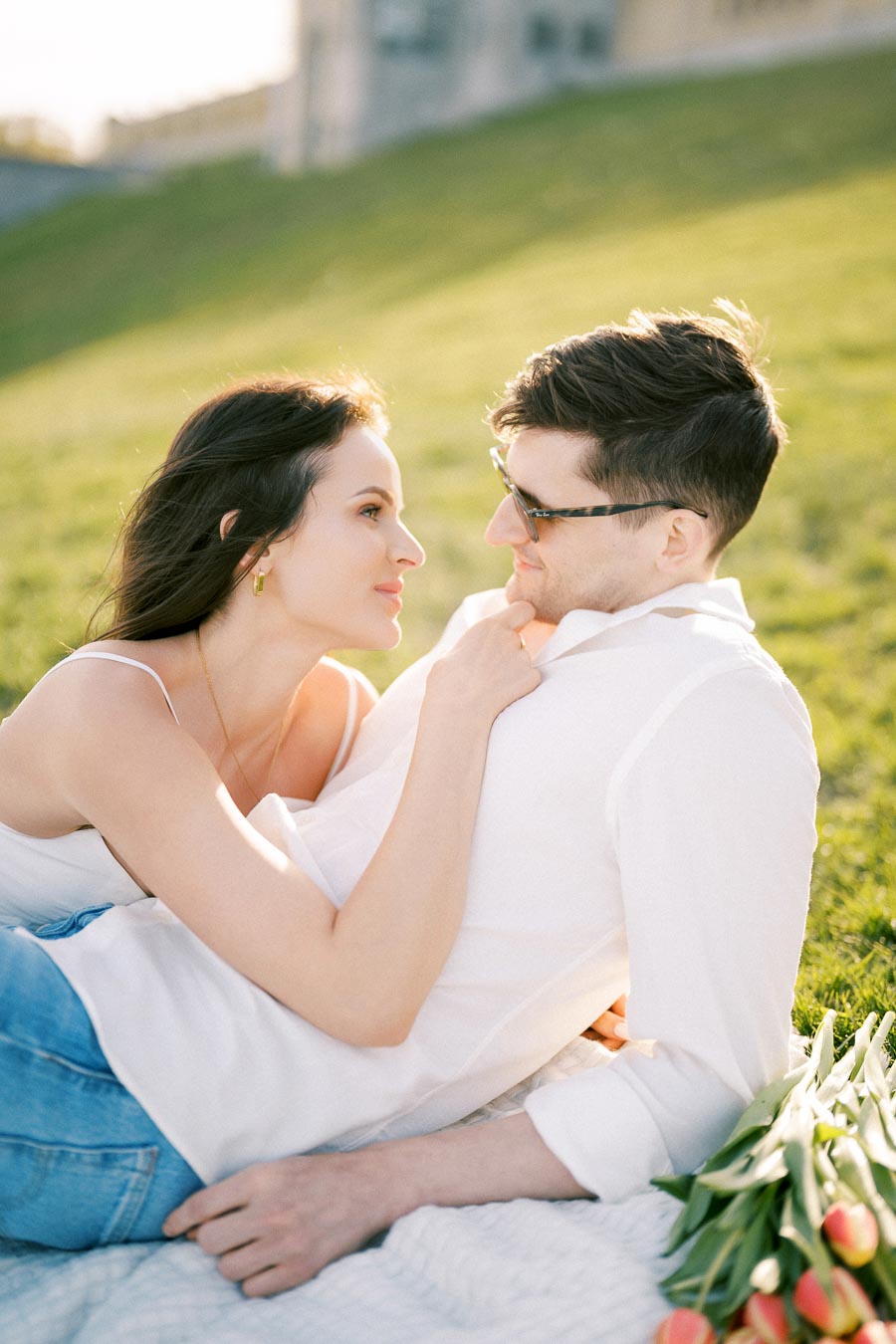 A couple enjoying a romantic picnic on a sunny day, lying on a blanket on the grass, with a bouquet of tulips beside them.