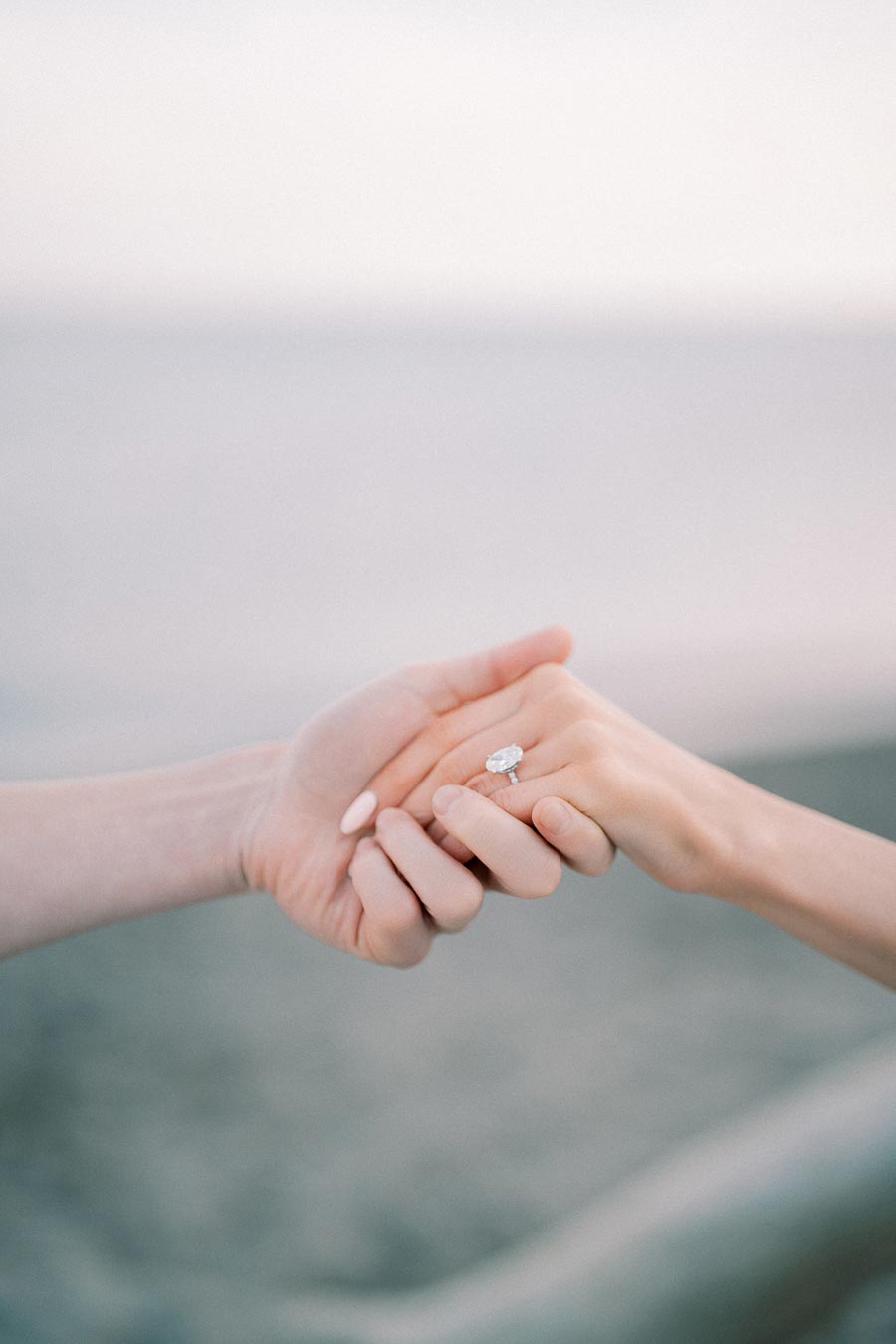 Hands gently holding with an engagement ring in focus against a soft, blurred background.