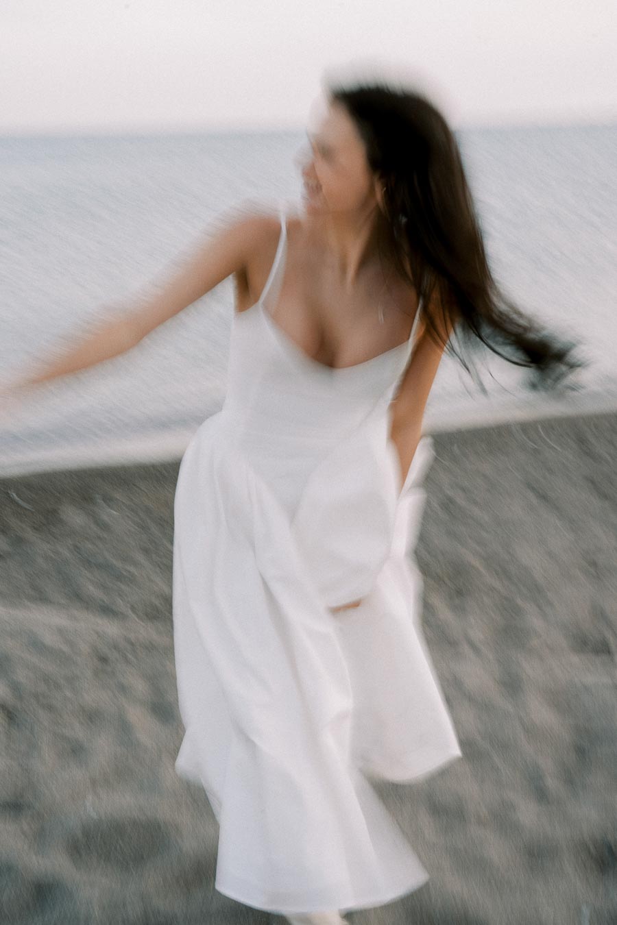 Blurred image of woman in white dress joyfully twirling by the sea.