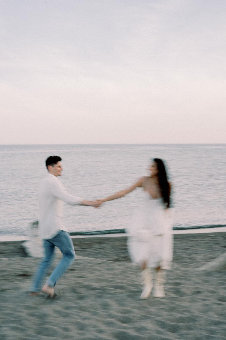 A couple holding hands and twirling on a sandy beach with the ocean in the background, captured in a blurred motion, conveying a sense of joy and movement.