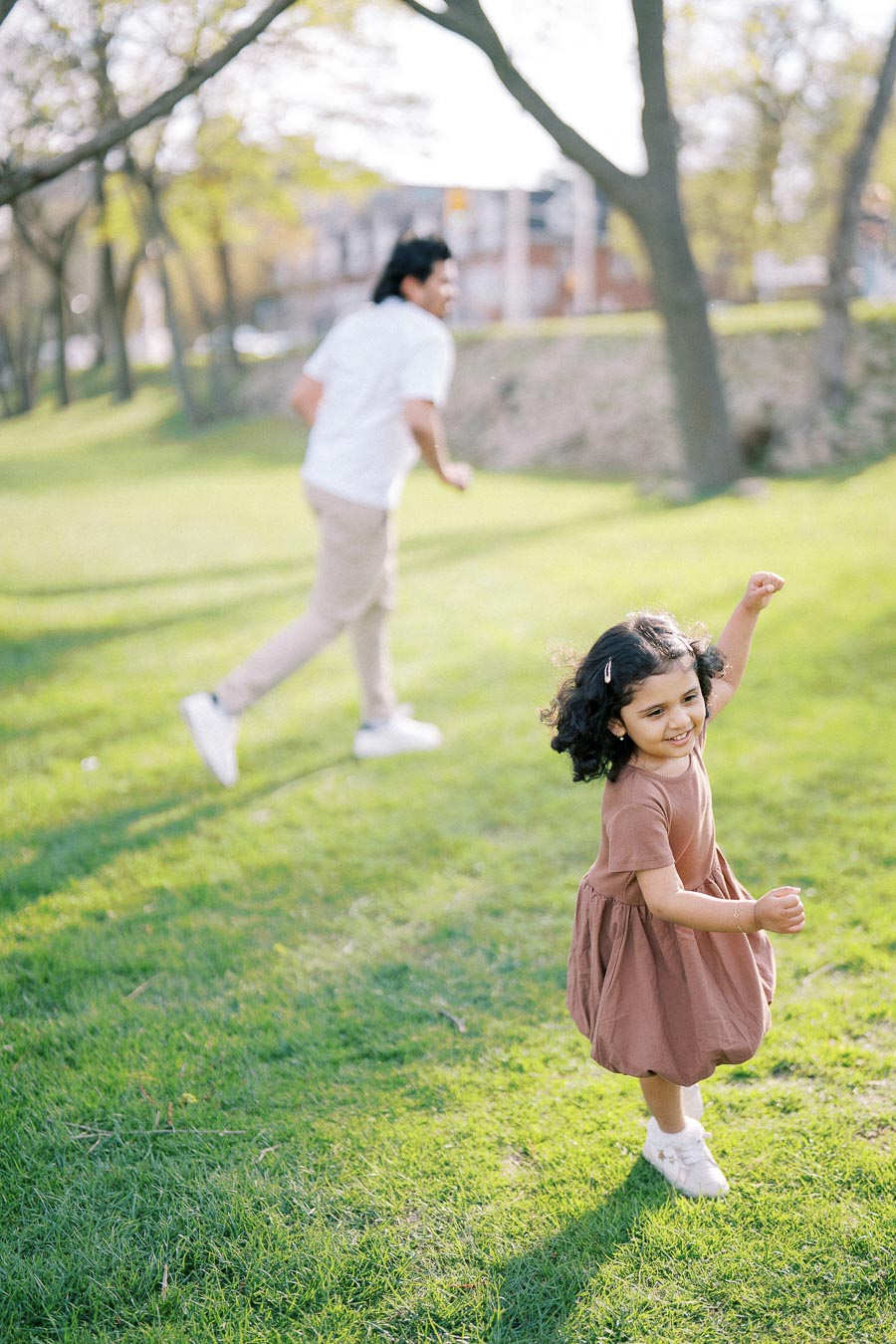 Father and daughter playing and running on a grassy field in a sunny park.