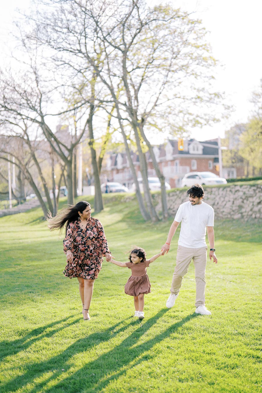 Happy family strolling through a sunlit park, with vibrant green grass and trees in the background.