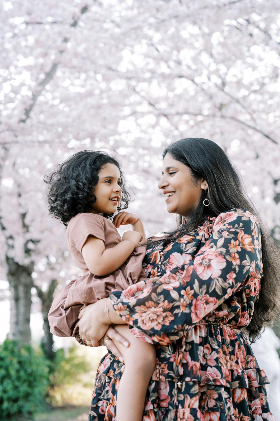 A mother and child smiling at each other surrounded by cherry blossom trees.