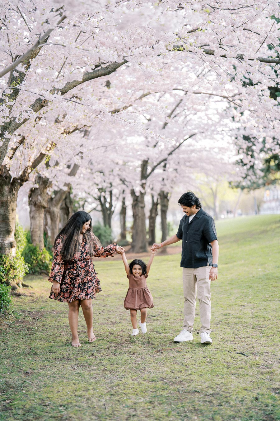 Family enjoying a walk under blooming cherry blossom trees, wearing stylish spring outfits in a park setting.