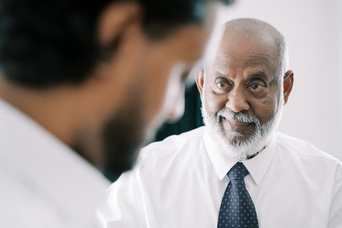 Elderly man in a white shirt and tie smiling at a younger person during a conversation. Business meeting or mentorship concept in a professional setting.