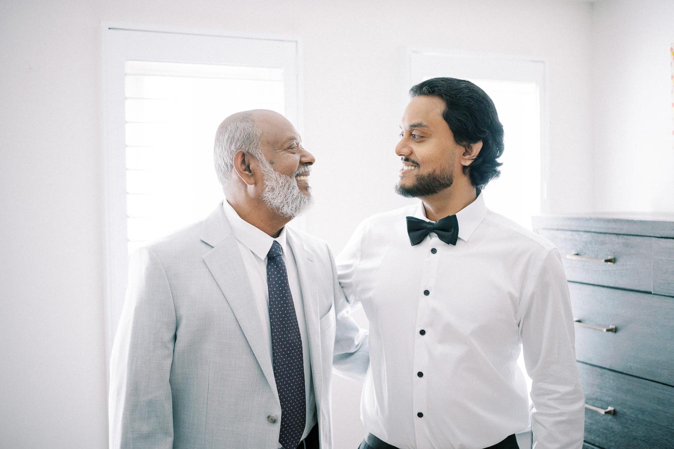 Father and son sharing a joyful moment, dressed in formal attire, standing in a well-lit room.