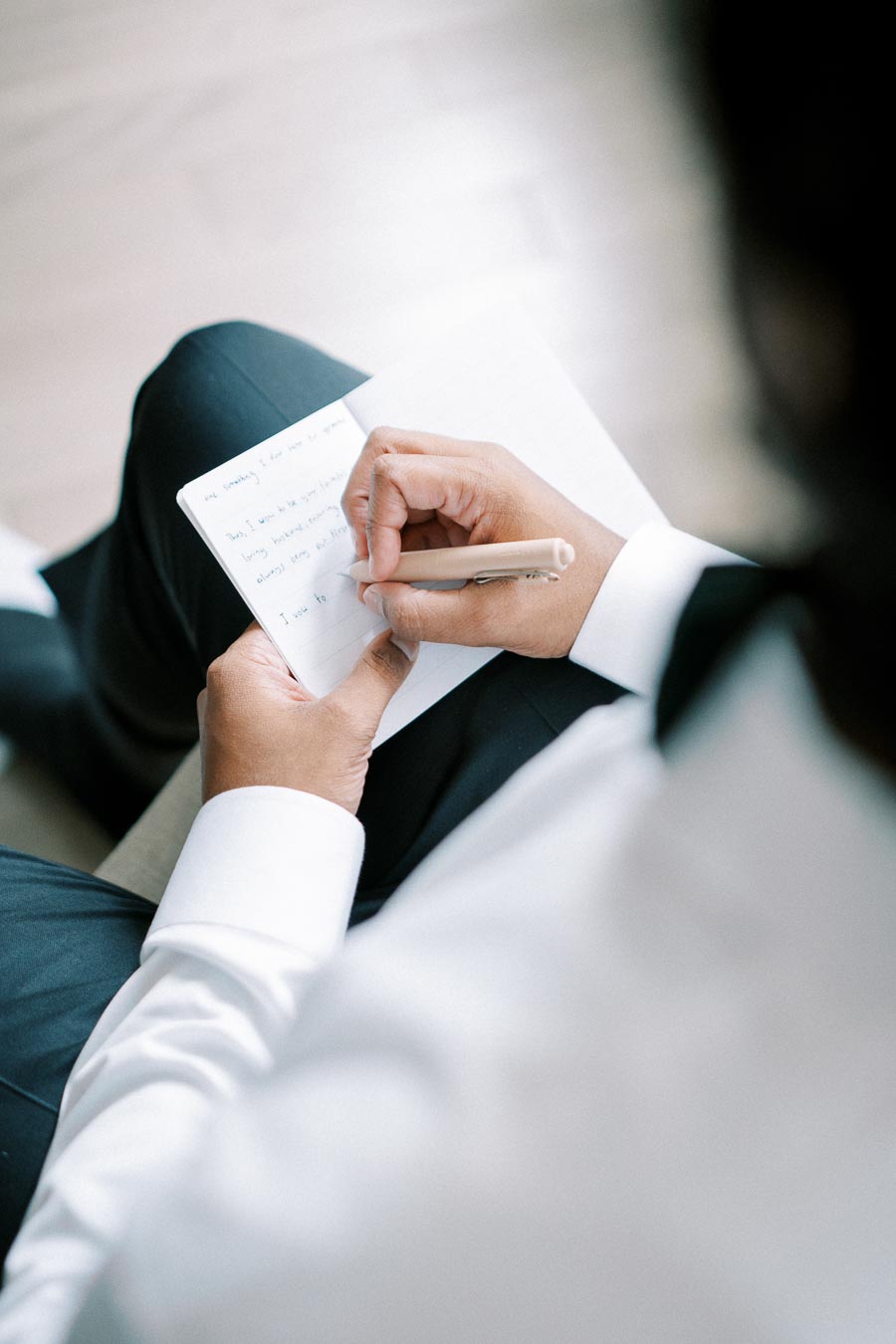 A person in a white shirt writing in a notebook with a pen, focusing on handwritten notes.