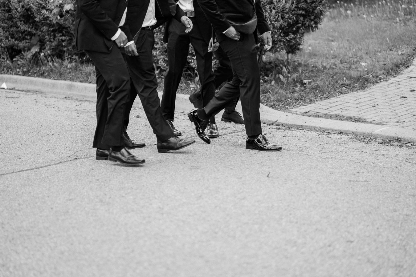 Black and white photo of four men in formal suits walking on a paved path.