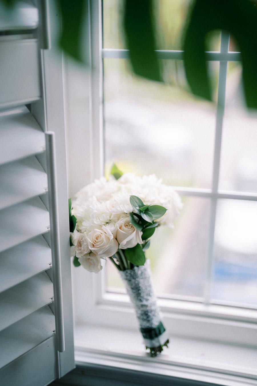 A bouquet of white roses and chrysanthemums wrapped in lace, resting on a sunlit windowsill, creating a serene and elegant ambiance.