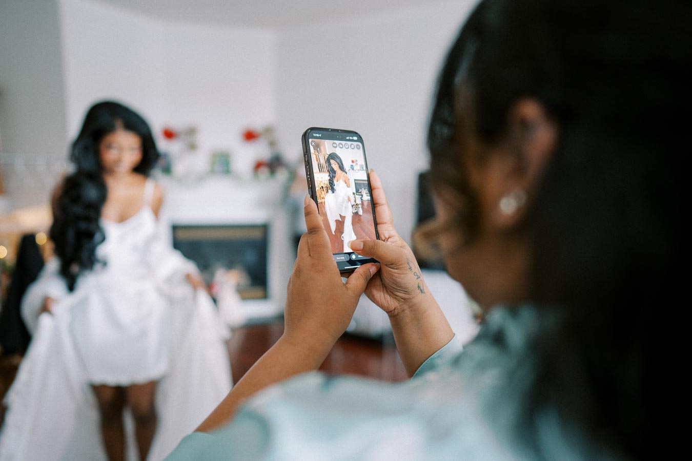 Young woman in a white robe being photographed on a smartphone, capturing a candid moment in a cozy, softly lit room.