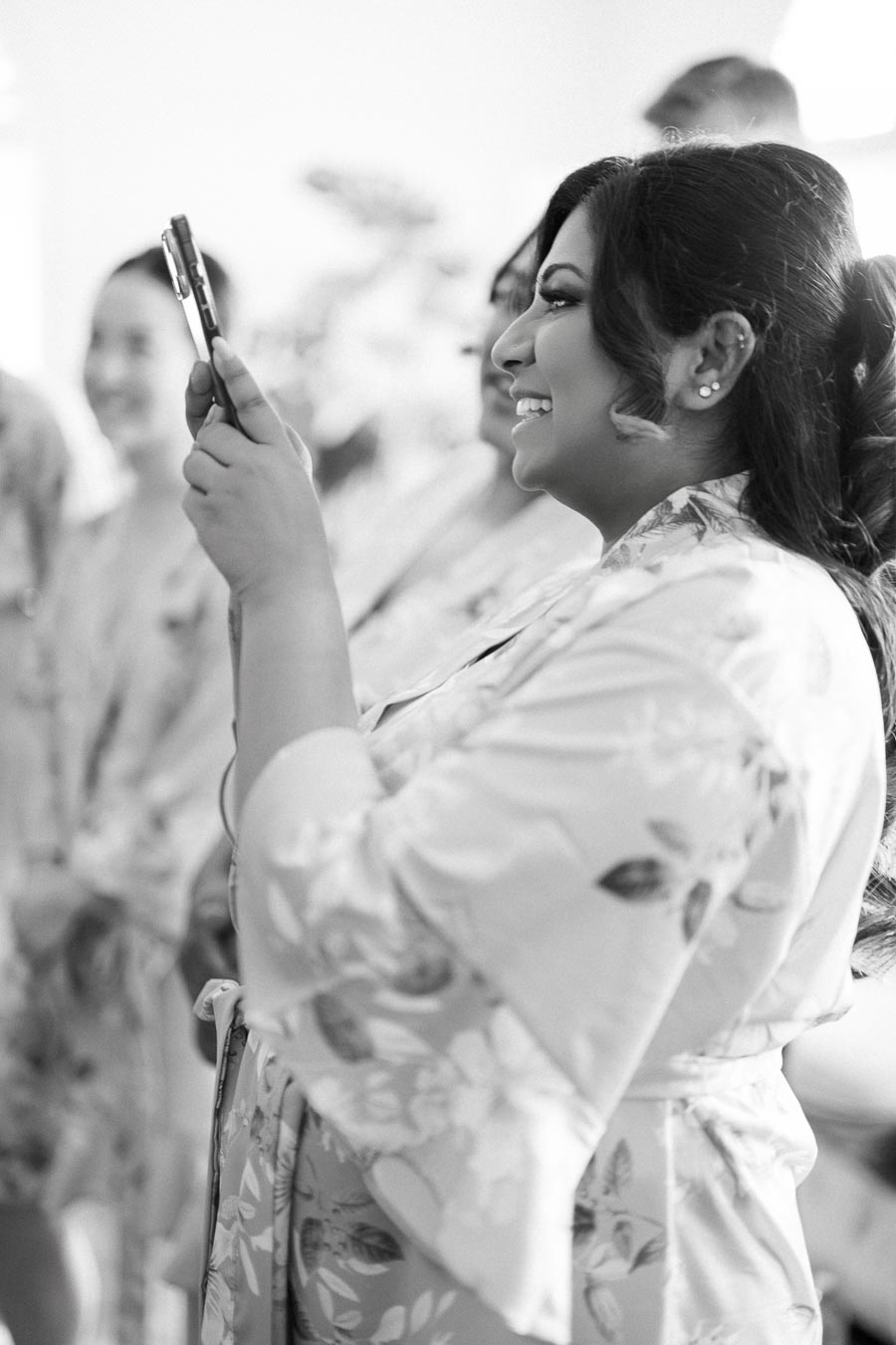 Smiling woman in floral robe taking a photo with smartphone, capturing a joyful moment.